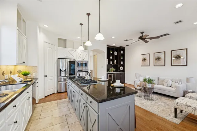 a kitchen with stainless steel appliances granite countertop a stove a sink dishwasher a refrigerator white cabinets and wooden floor