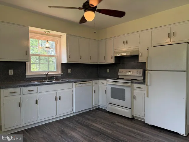 a kitchen with granite countertop white cabinets white appliances a sink and a window