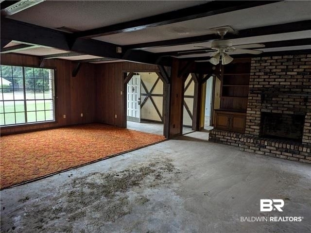 3817 Lansdowne Circle Mobile, AL 36693 - Photo 11 of 16 Unfurnished living room with wood walls, a fireplace, beam ceiling, and ceiling fan