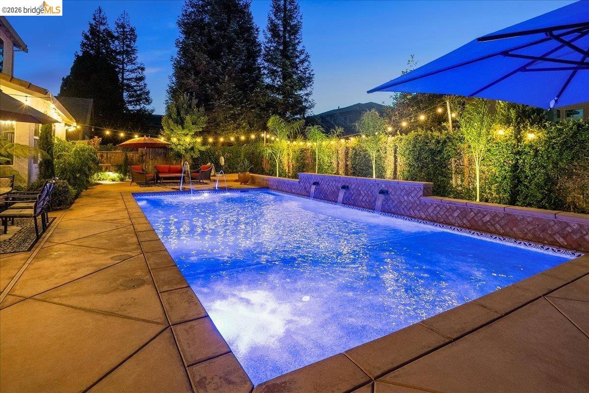 653 Bouma Lane Ripon, CA 95366 - Photo 33 of 39 Swimming pool with integrated water features, concrete decking, perimeter privacy landscaping, and string lighting