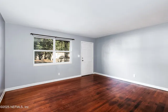 a view of an empty room with wooden floor and a window