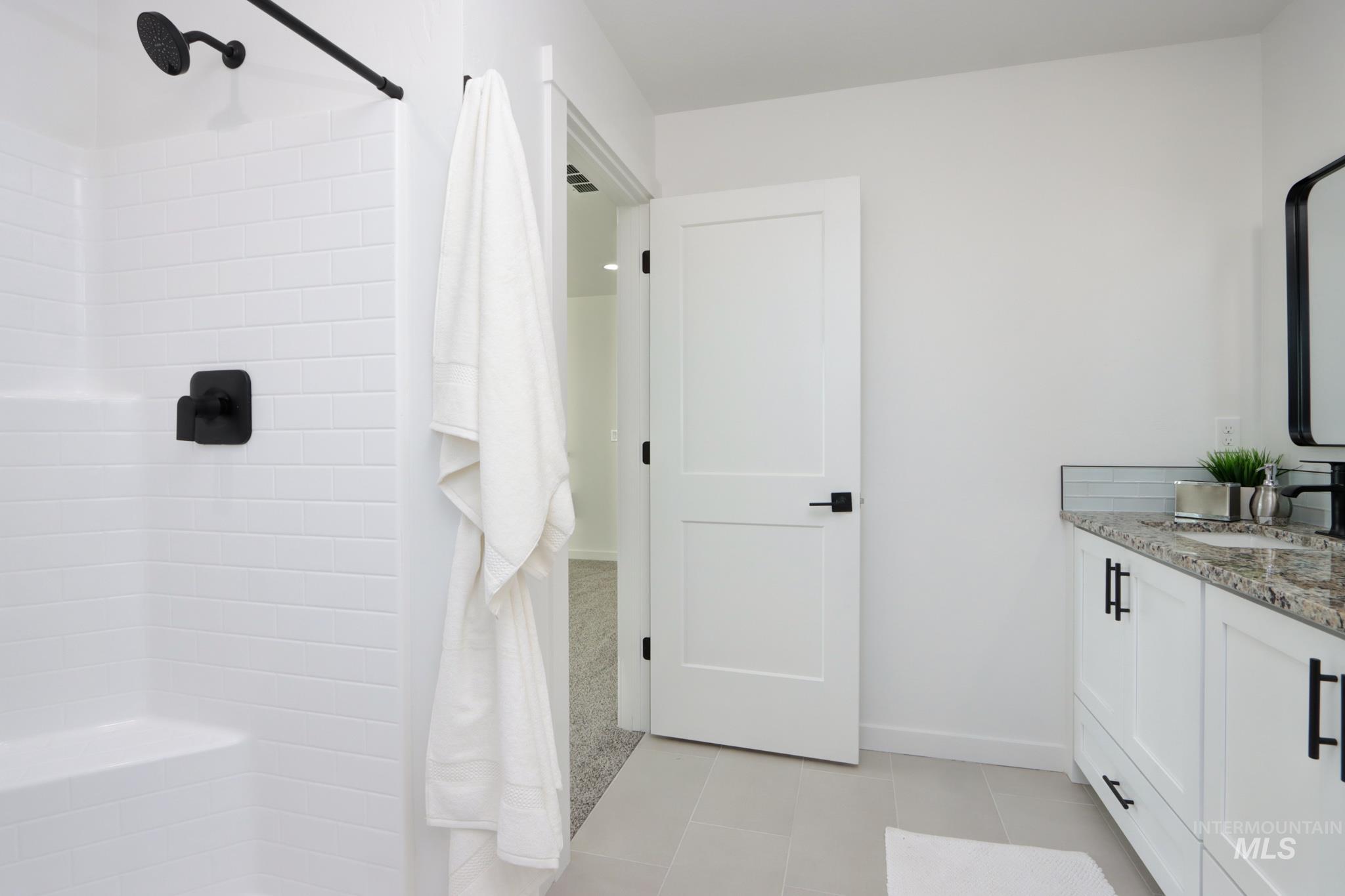 950 Campbell Street Vale, OR 97918 - Photo 24 of 37 Bathroom featuring a shower with white subway tile surround and matte black fixtures, a white vanity with a stone countertop and rectangular undermount sink, a framed mirror, and light-toned tile flooring