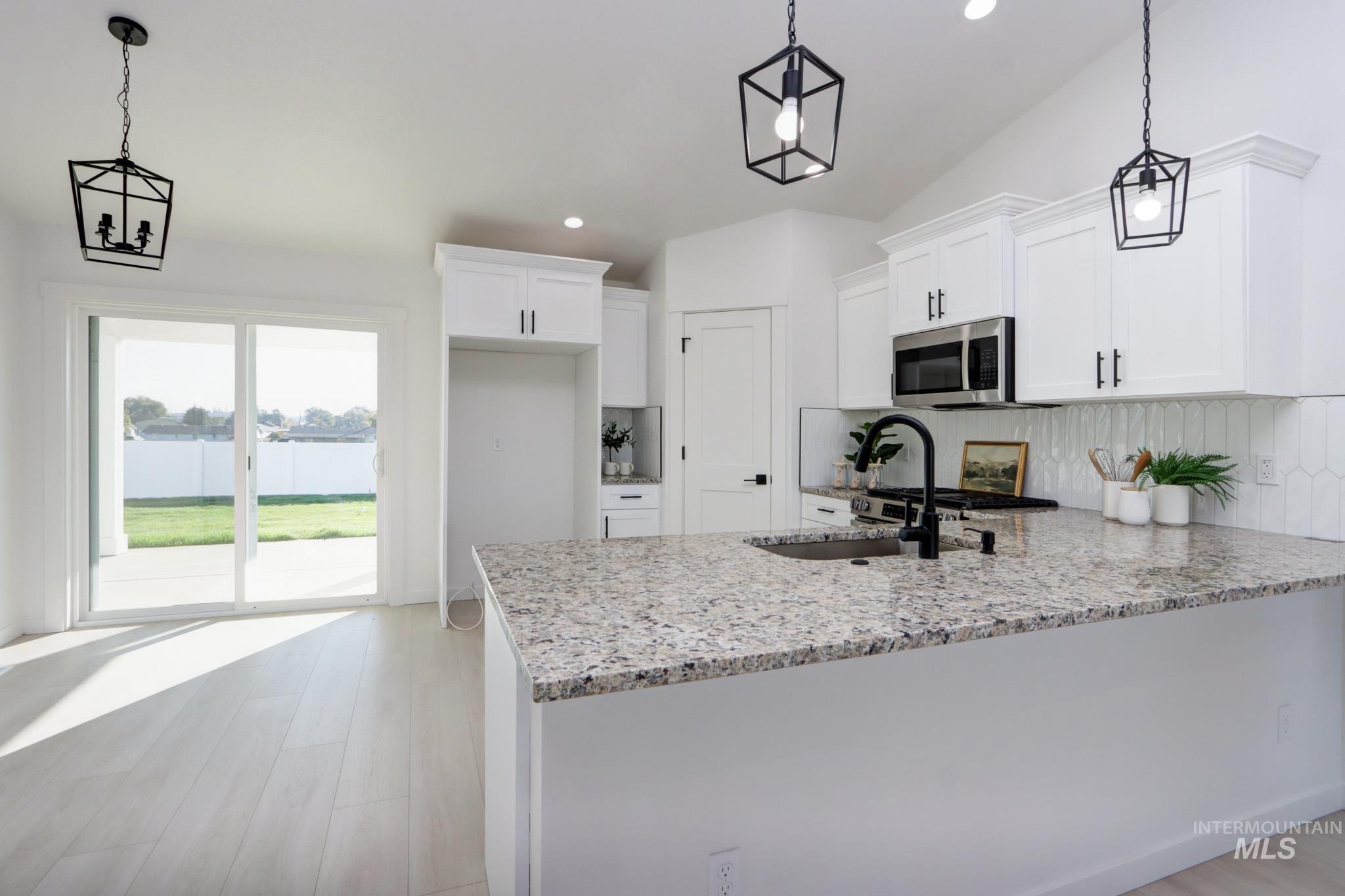 950 Campbell Street Vale, OR 97918 - Photo 8 of 37 Kitchen featuring white cabinetry, a large central island with a speckled countertop, a stainless steel microwave, black hardware, and a white picket tile backsplash