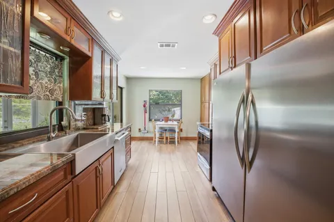 a kitchen with stainless steel appliances granite countertop a refrigerator a sink a stove and a wooden cabinets