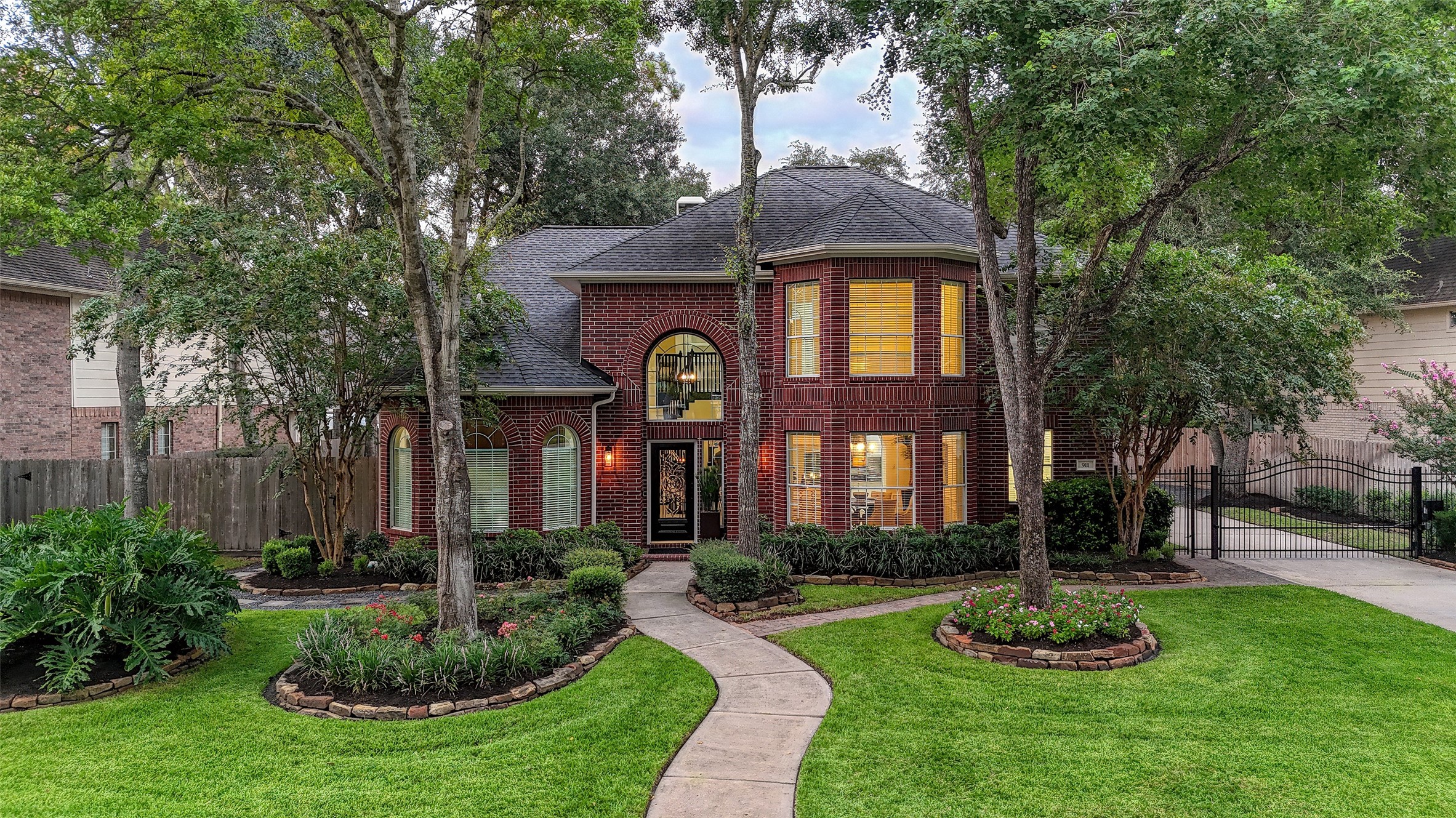 911 Chisel Point Drive Houston, TX 77094 - Photo 2 of 50 Stunning two-story brick home with striking architectural details, framed by mature trees and lush landscaping. A winding walkway leads to the elegant front entry with decorative glass doors and a soaring arched window above.