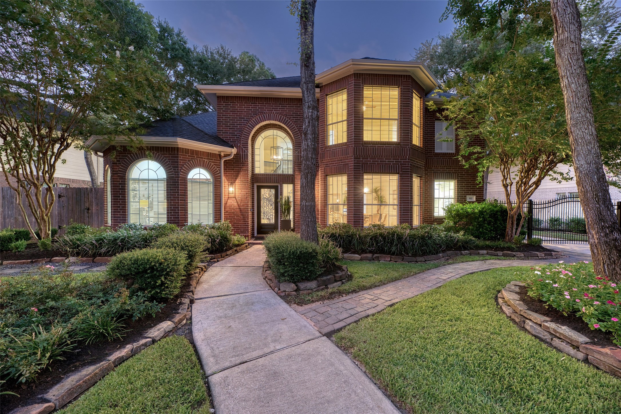 911 Chisel Point Drive Houston, TX 77094 - Photo 39 of 50 The home’s brick façade glows warmly in the evening light, showcasing arched windows and a grand entryway with decorative glass door. A curved walkway winds through lush landscaping, leading you right to the front door.