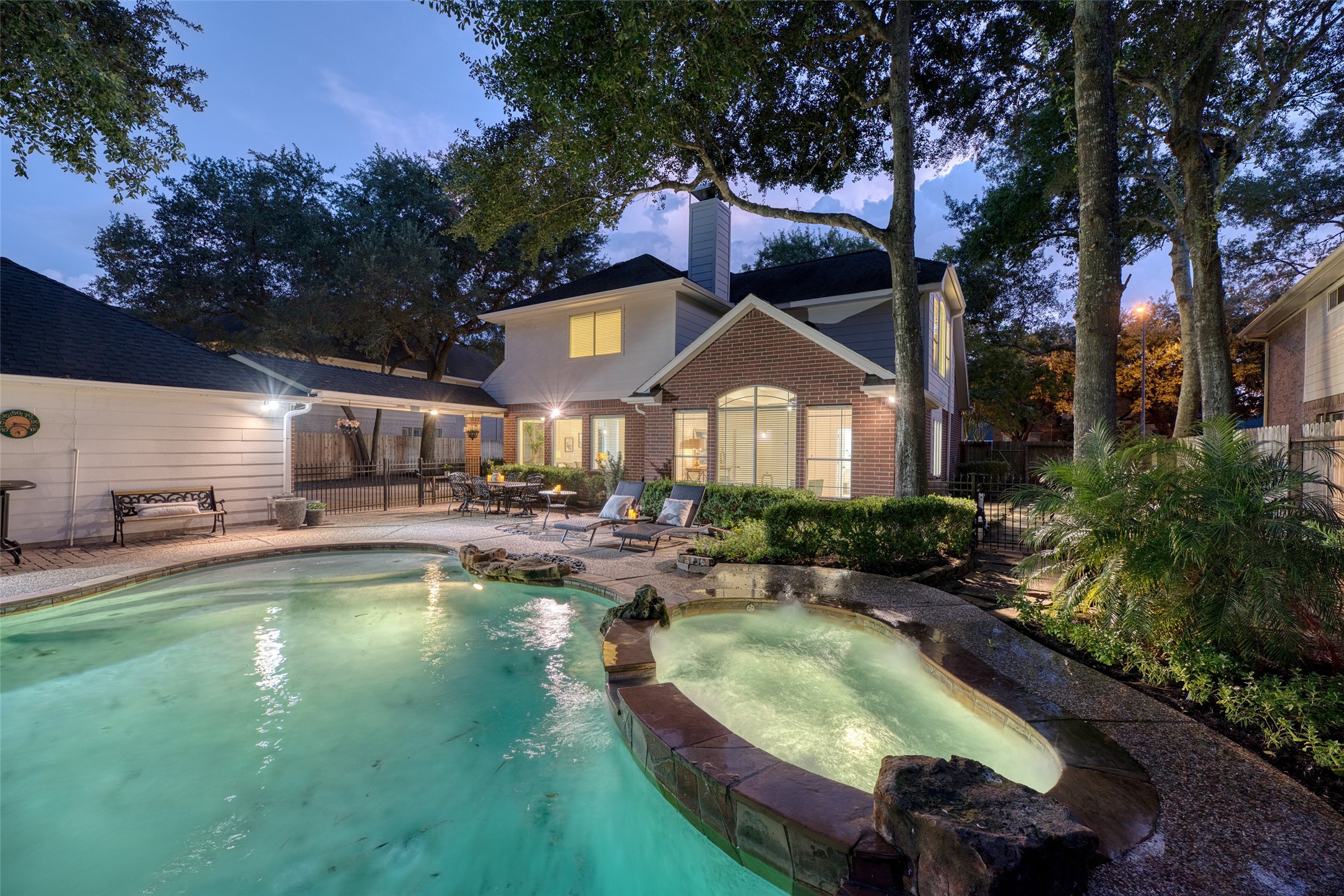 911 Chisel Point Drive Houston, TX 77094 - Photo 41 of 50 Enjoy resort-inspired living with a heated spa cascading into the pool, framed by stone accents and greenery. The expansive patio offers multiple seating areas for dining or lounging, all set against the beautiful twilight sky.