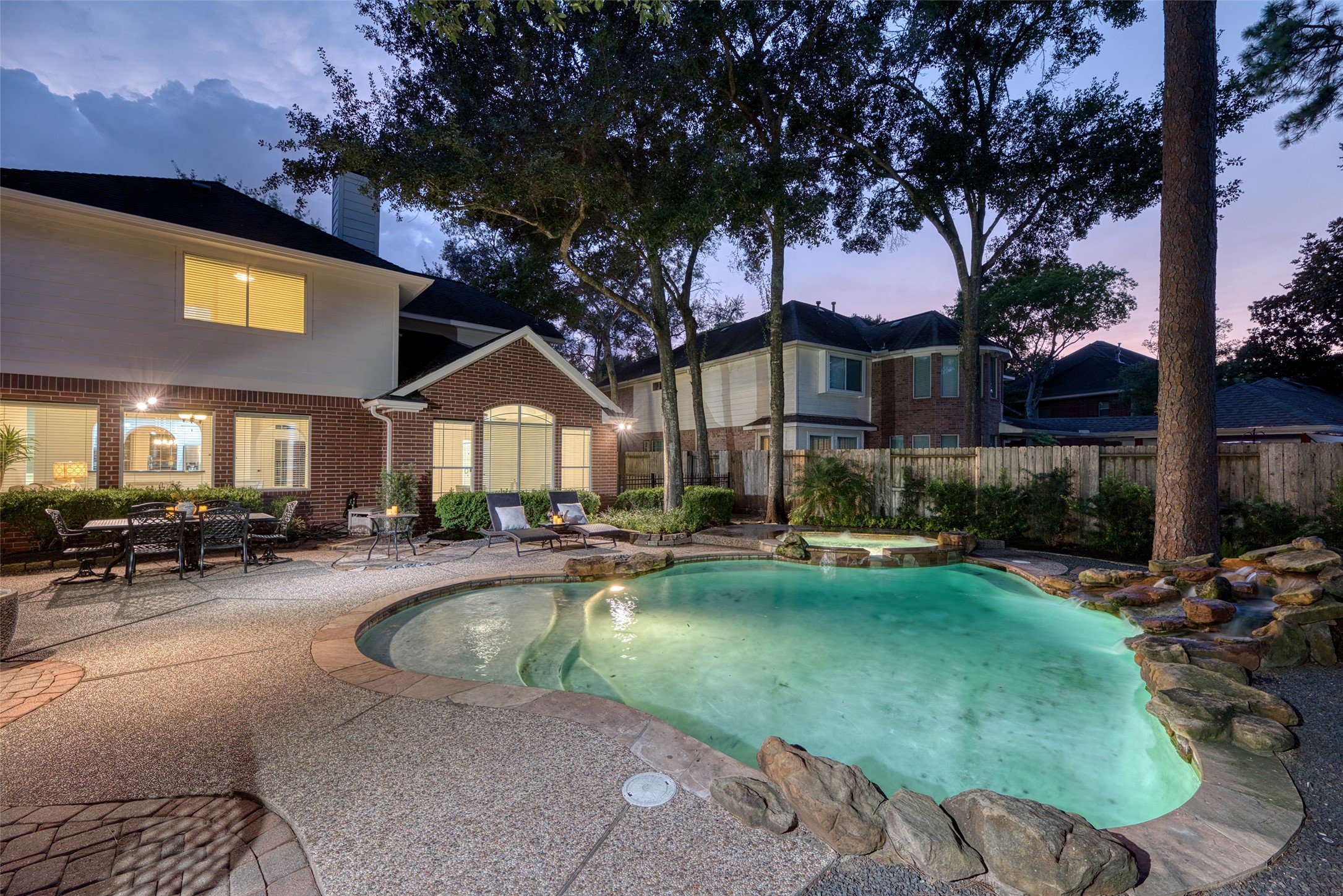 911 Chisel Point Drive Houston, TX 77094 - Photo 45 of 50 Under the glow of evening lights, the backyard transforms into a serene retreat with a sparkling pool, soothing rock waterfall, and integrated spa. Surrounded by mature trees and lush landscaping, this private escape is perfect for unwinding or entertaining.