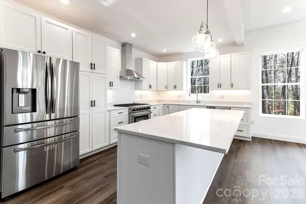 a kitchen with stainless steel appliances granite countertop a refrigerator a sink dishwasher a stove and white cabinets with wooden floor