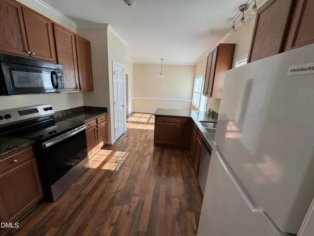 a kitchen with granite countertop a refrigerator a stove top oven and wooden floor