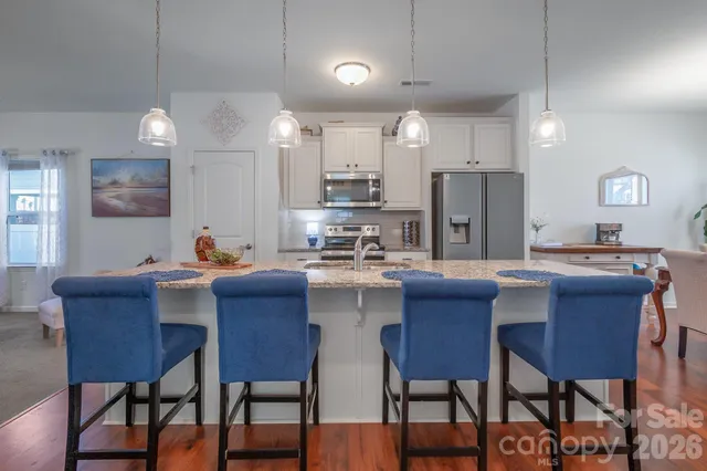 a kitchen with stainless steel appliances granite countertop a dining table chairs and a refrigerator