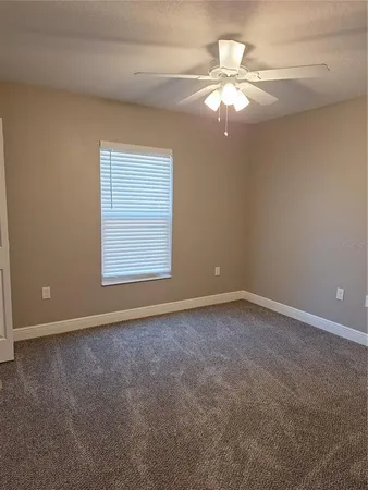 an empty room with a chandelier fan and windows