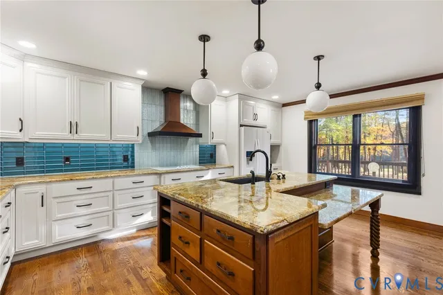 a kitchen with kitchen island granite countertop a stove a sink a refrigerator and white cabinets with wooden floor