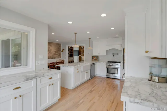 a large kitchen with stainless steel appliances kitchen island granite countertop a stove a sink a refrigerator and white cabinets with wooden floor