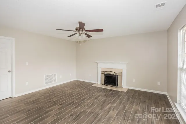 a view of an empty room with wooden floor a fireplace and a window