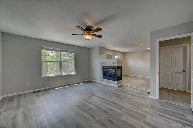 an empty room with wooden floor fan and windows