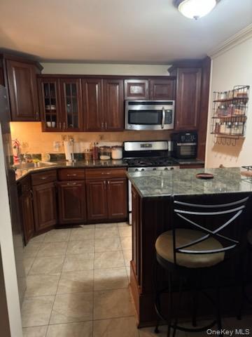 23 Notingham Circle, Unit 23 Peekskill, NY 10566 - Photo 7 of 12 Kitchen with a kitchen breakfast bar, stainless steel appliances, dark brown cabinets, glass insert cabinets, and dark stone countertops