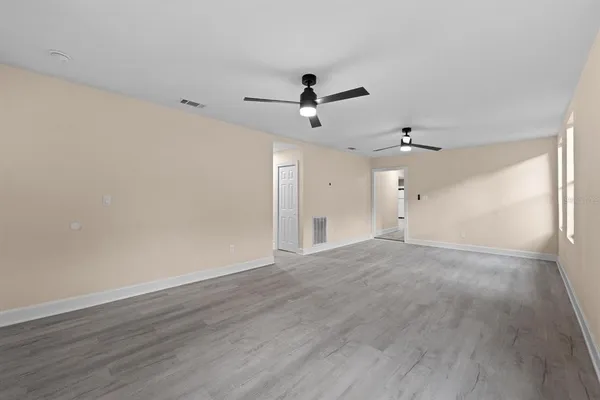 an empty room with wooden floor ceiling fan and windows