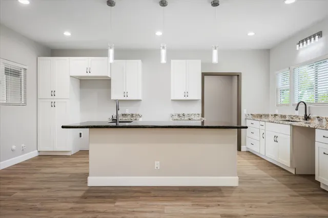 a large kitchen with stainless steel appliances granite countertop a large stove a sink a refrigerator and white cabinets with wooden floor