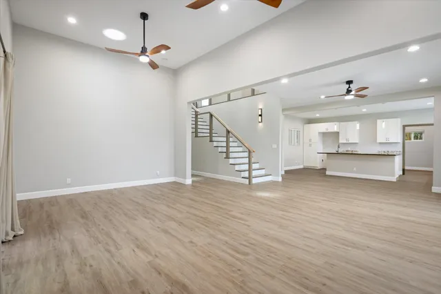 a view of an empty room with wooden floor kitchen view and a window