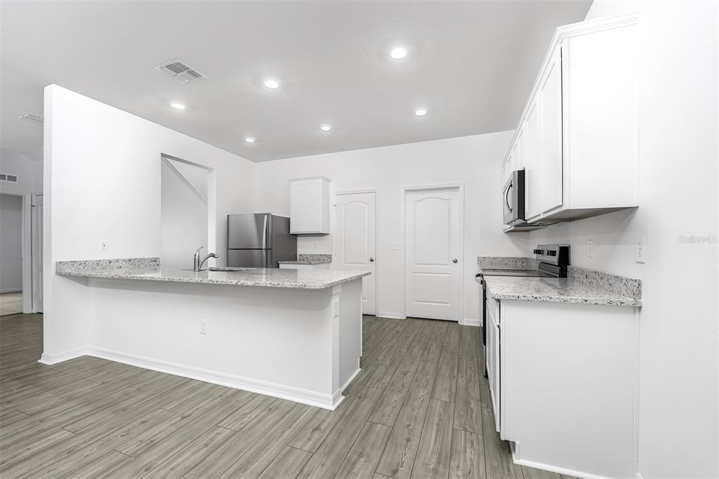 13340 Tula Loop Astatula, FL 34705 - Photo 5 of 21 a kitchen with stainless steel appliances granite countertop a sink stove and white cabinets with wooden floor