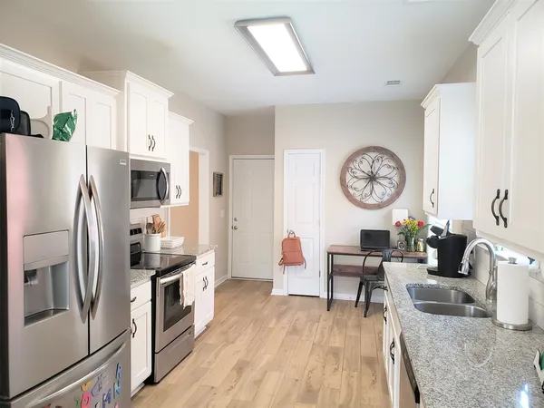 a kitchen with stainless steel appliances granite countertop a refrigerator a sink dishwasher a stove and white countertops with wooden floor