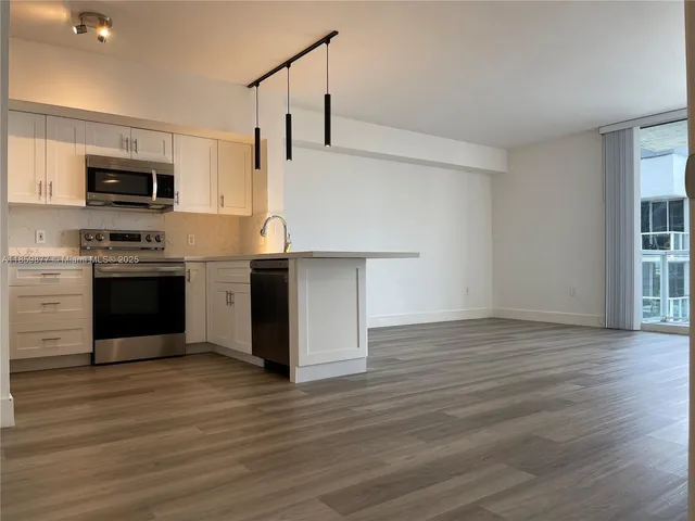 a view of kitchen with stainless steel appliances granite countertop a stove top oven a sink and white cabinets with wooden floor