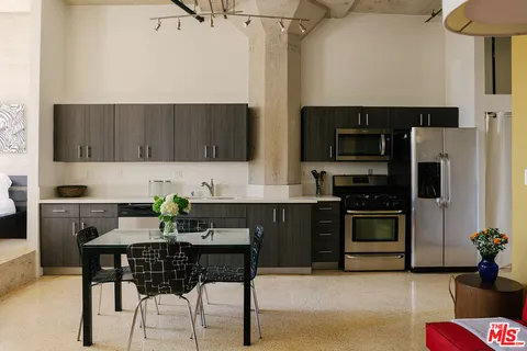 a kitchen with stainless steel appliances a stove a sink dishwasher a refrigerator with a dining table and chairs