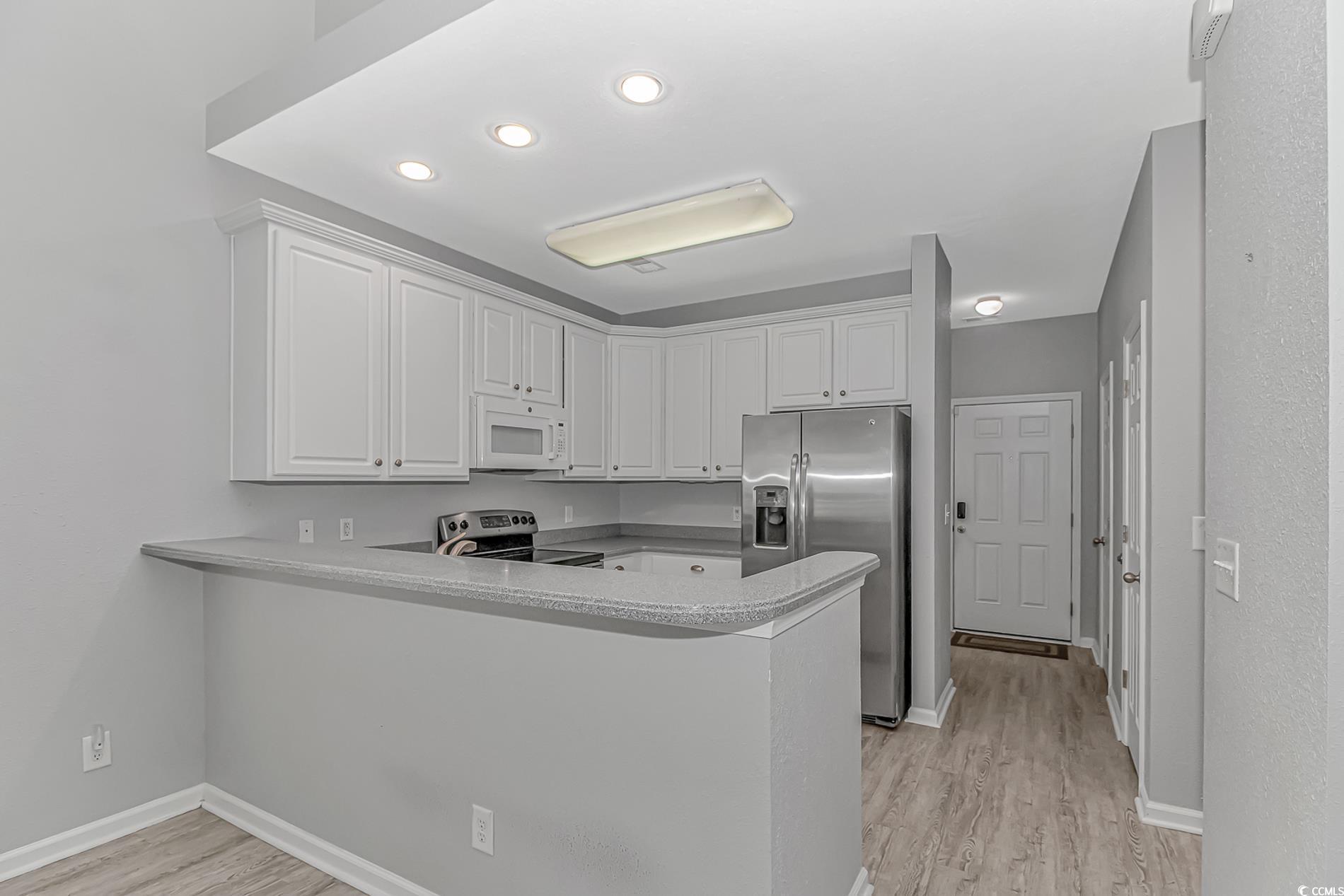 751 Painted Bunting Drive, Unit E Murrells Inlet, SC 29576 - Photo 12 of 40 Kitchen featuring stainless steel appliances, a peninsula, light wood-type flooring, white cabinetry, and baseboards