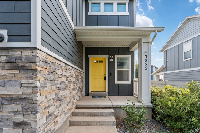 7822 North Copperbend Road Eagle Mountain, UT 84005 - Photo 6 of 46 Exterior featuring stone facade, dark siding, concrete steps, a covered porch, and a vibrant yellow entry door