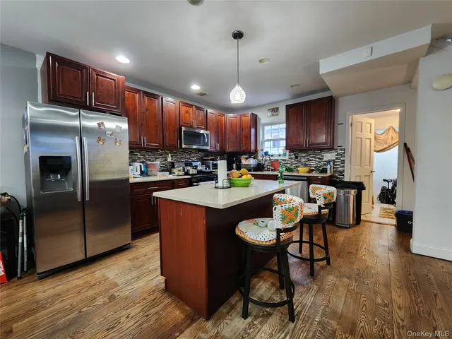 a kitchen with stainless steel appliances granite countertop a refrigerator a sink dishwasher a stove and a dining table with wooden floor