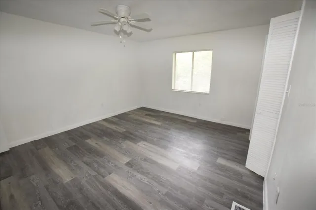 an empty room with wooden floor fan and windows
