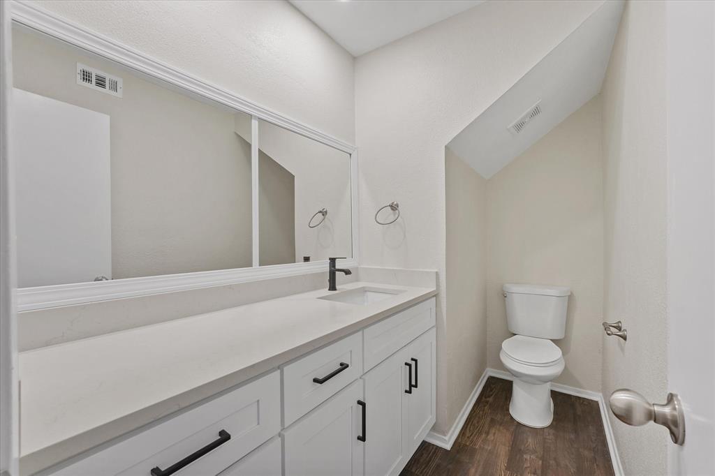 4007 Ridgebrook Drive Arlington, TX 76015 - Photo 11 of 18 Bathroom featuring a white vanity with black hardware, a large wall-mounted mirror with decorative trim, a white countertop, a black single-handle faucet, and wood-finish flooring