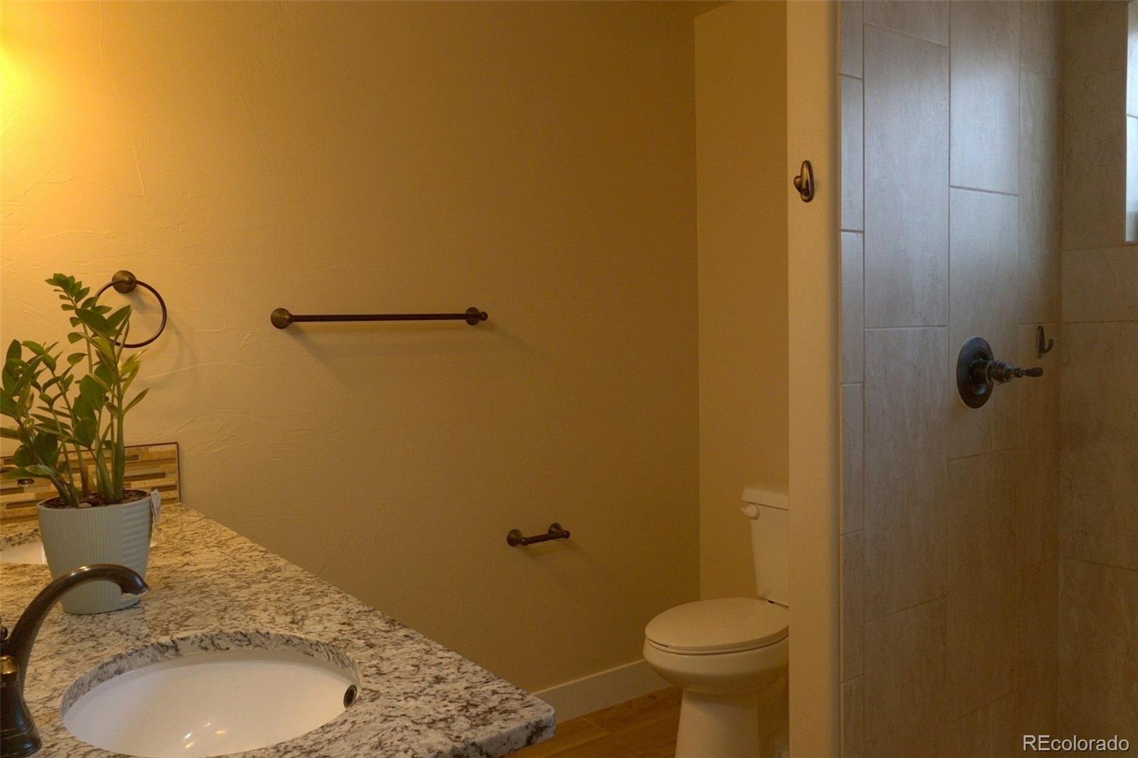 1113 Bison Way Wiggins, CO 80654 - Photo 11 of 20 a bathroom with a granite countertop toilet and a sink
