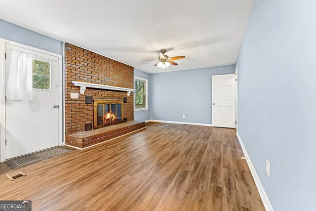 a view of an empty room with wooden floor fireplace and a window
