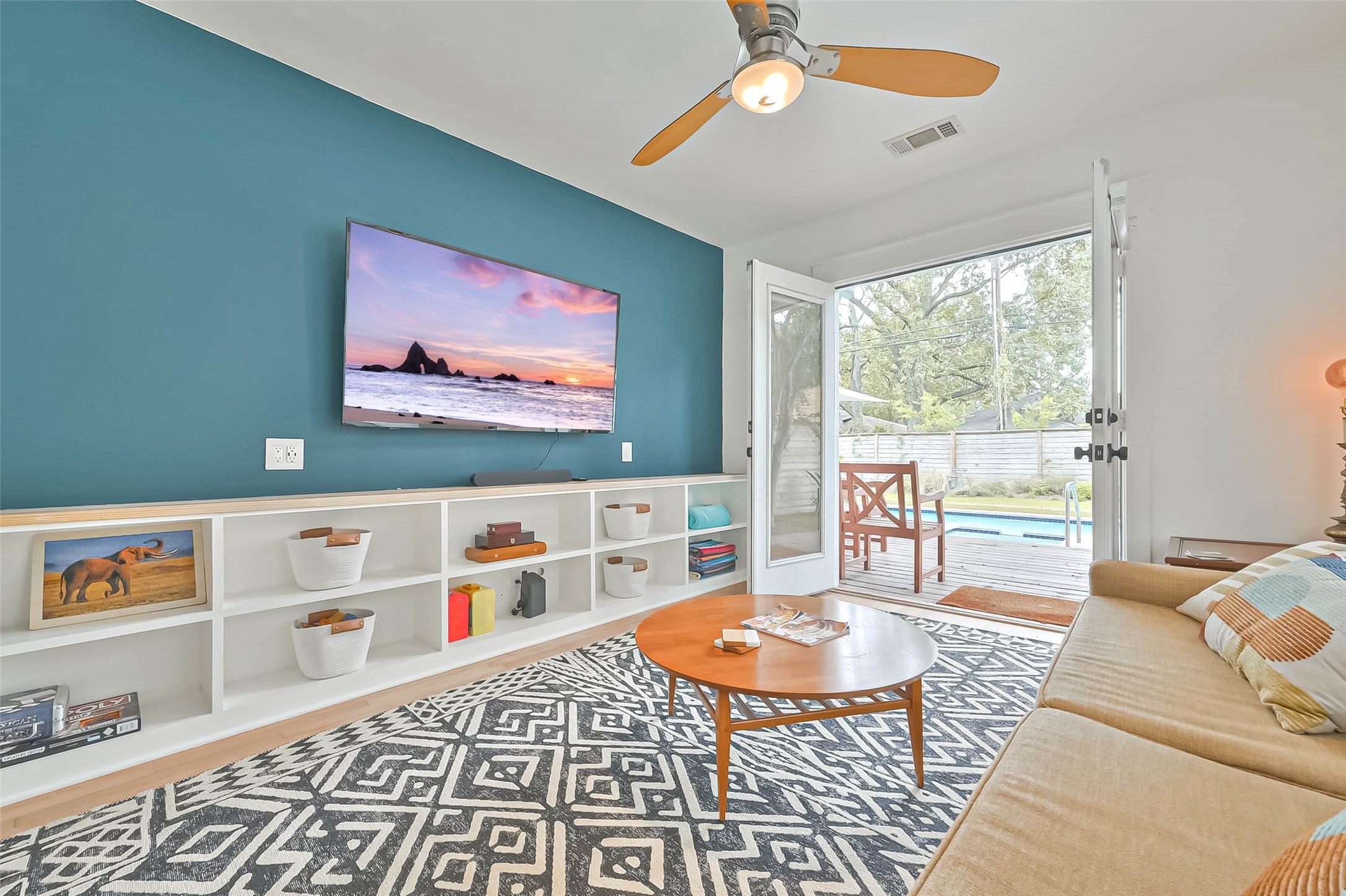 412 Sue Street Houston, TX 77009 - Photo 7 of 19 This inviting light filled flex room/den has built in bookcases and a teal accent wall. Open double doors lead to a deck and a clear view of a backyard pool, enhancing the indoor-outdoor flow. Ideal for relaxation and entertainment.