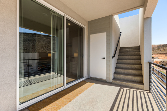 839 Walker Way St. George, UT 84770 - Photo 25 of 32 Exterior balcony featuring a sliding glass door, a pedestrian door, a staircase with a black metal handrail, and a black metal balcony railing