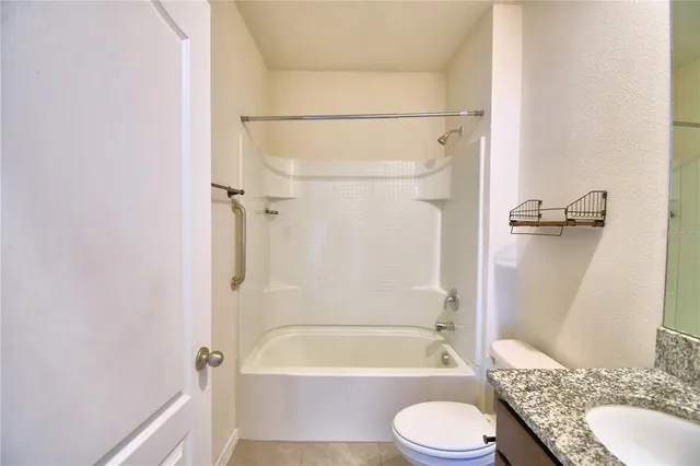 a bathroom with a granite countertop bathtub shower sink vanity and toilet