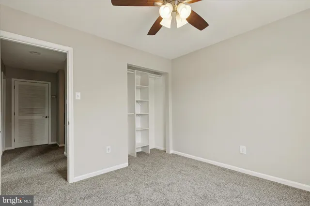 an empty room with a chandelier fan and kitchen view