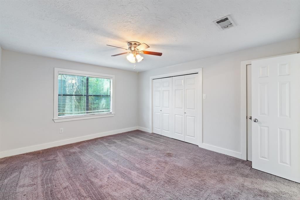 1305 Idylwild Street Houston, TX 77009 - Photo 25 of 31 This is a bright, carpeted bedroom featuring a ceiling fan, a large window with blinds, and ample closet space with white double doors.