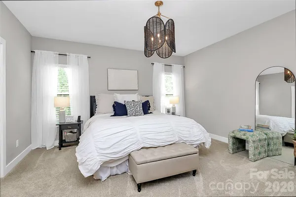 a spacious bedroom with a bed a chandelier and mirror