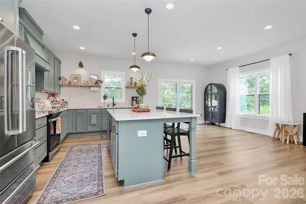a kitchen with stainless steel appliances granite countertop a refrigerator a sink dishwasher a dining table and chairs with wooden floor