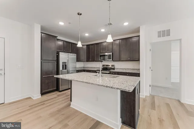 a kitchen with granite countertop stainless steel appliances a sink dishwasher a refrigerator a stove top oven and cabinets