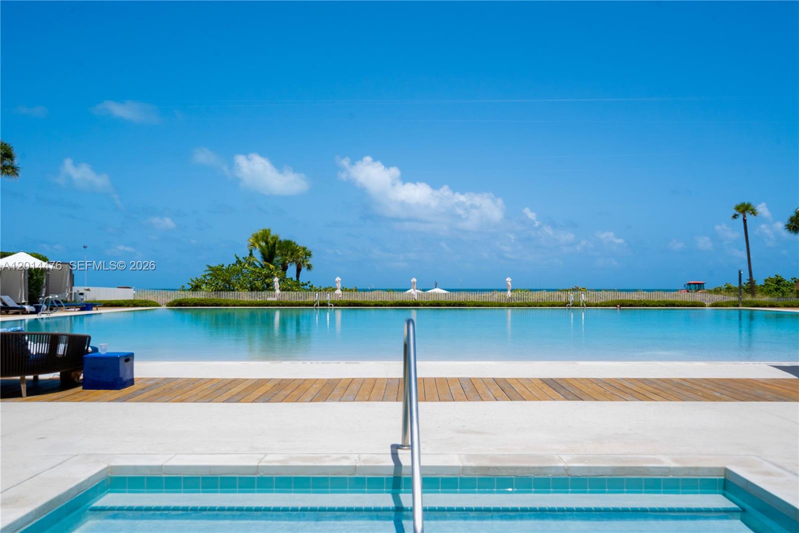 360 Ocean Drive, Unit 1106S Key Biscayne, FL 33149 - Photo 36 of 67 Pool and Spa Area – This view highlights the spa steps leading toward the expansive pool, with palm trees and ocean views in the background. The surrounding lounge areas and open sky enhance the resort-inspired feel.