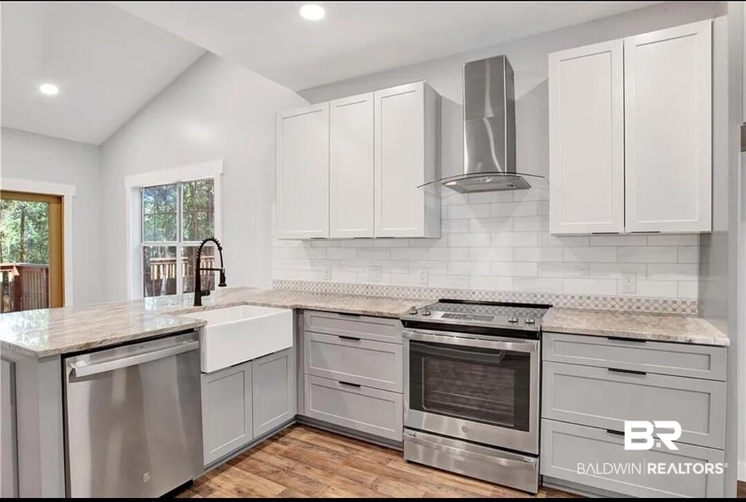 632 Ridgewood Drive Daphne, AL 36526 - Photo 11 of 36 Kitchen with appliances with stainless steel finishes, sink, light stone counters, kitchen peninsula, and wall chimney range hood