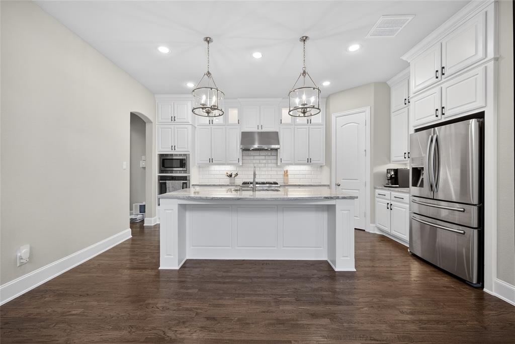 1039 Stephen Street Allen, TX 75013 - Photo 11 of 40 Kitchen featuring arched walkways, white cabinetry, stainless steel appliances, light stone counters, and a kitchen island with sink