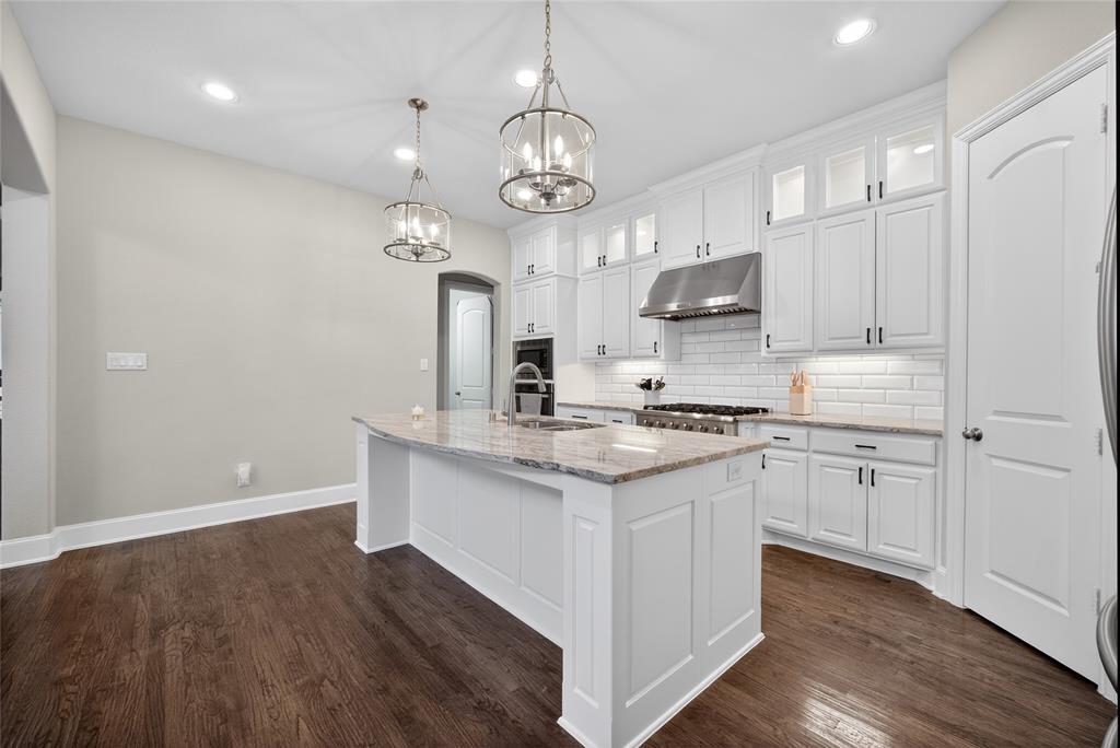 1039 Stephen Street Allen, TX 75013 - Photo 12 of 40 Kitchen with white cabinetry, light stone counters, glass fronted cabinets, decorative backsplash, and an island with sink
