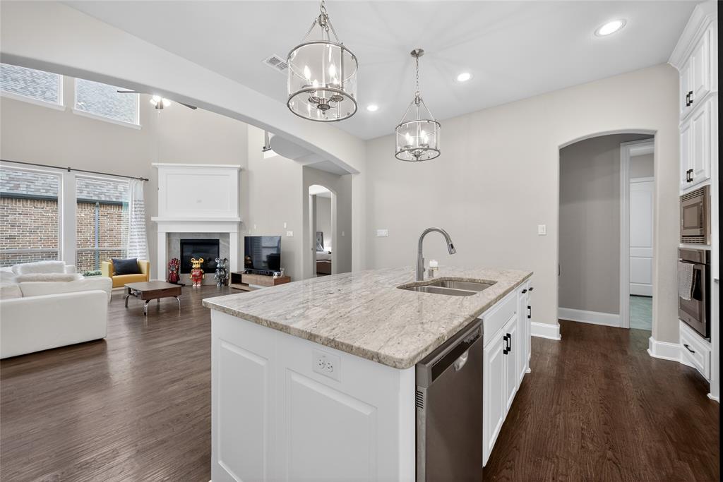 1039 Stephen Street Allen, TX 75013 - Photo 13 of 40 Kitchen with stainless steel appliances, a fireplace, a center island with sink, arched walkways, and light stone countertops