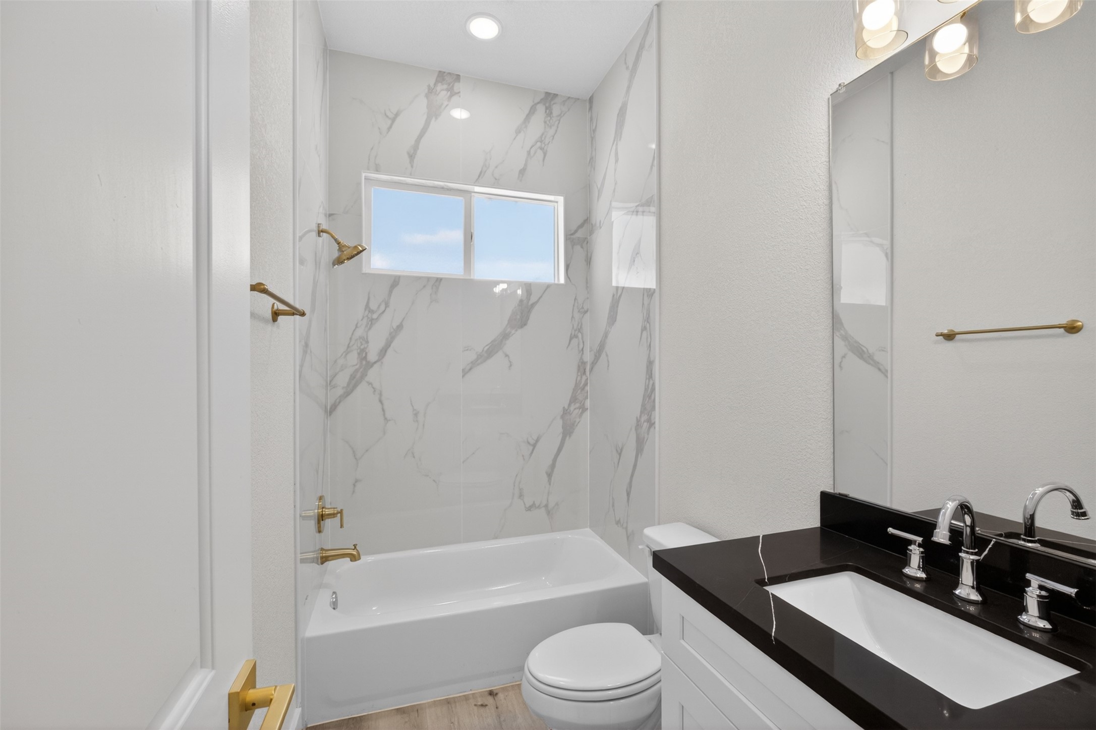 5906 St Augustine Street, Unit F Houston, TX 77021 - Photo 22 of 34 Full bathroom with a tub-shower combination, marble-look surround, black vanity top, and gold-tone fixtures.