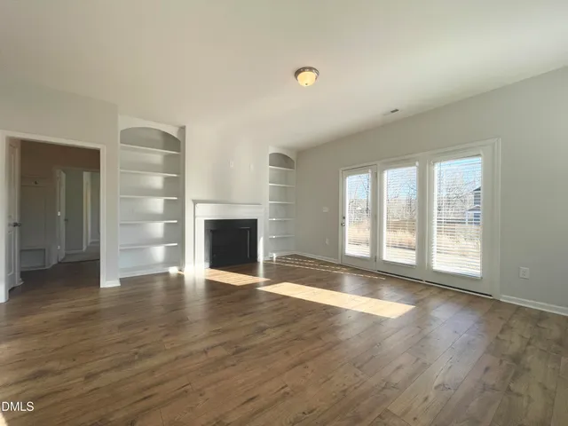 an empty room with wooden floor fireplace and windows